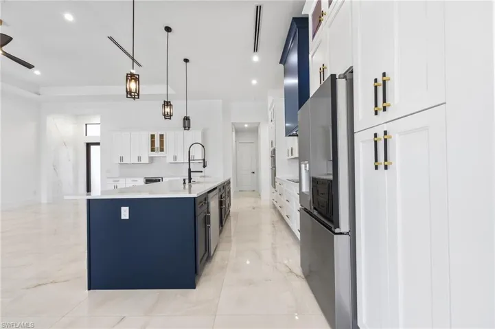 Kitchen featuring a contrasting navy and white cabinetry scheme, large center island with a high-arc faucet, stainless steel refrigerator, stone-finish flooring, and industrial-style pendant lighting