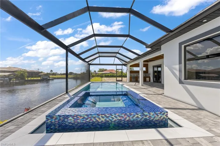Screened lanai featuring a built-in pool and raised spa with iridescent glass tile, paved deck, and water-facing exterior