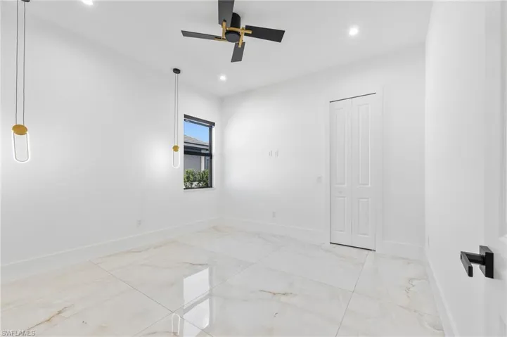 Large-format tile flooring with veining detail, modern matte black ceiling fan, dual linear pendant lighting, and bi-fold closet doors