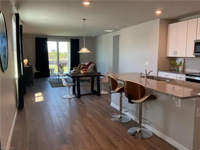 Kitchen featuring stone counters, dark wood-style flooring, a sink, stainless steel microwave, and tasteful backsplash