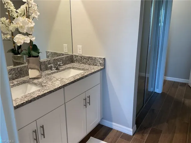 Full bath with a sink, baseboards, double vanity, and wood tiled floor