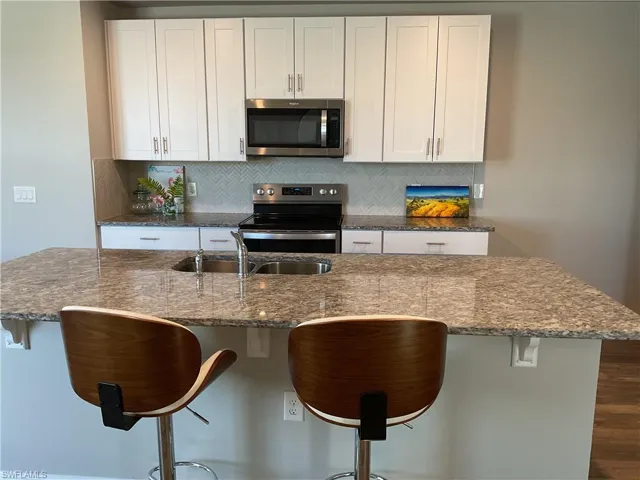 Kitchen with a kitchen island with sink, tasteful backsplash, dark stone counters, appliances with stainless steel finishes, and white cabinets