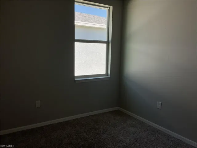 Empty room featuring plenty of natural light, baseboards, and dark carpet