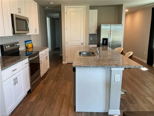Kitchen with dark wood-type flooring, a sink, backsplash, appliances with stainless steel finishes, and stone counters