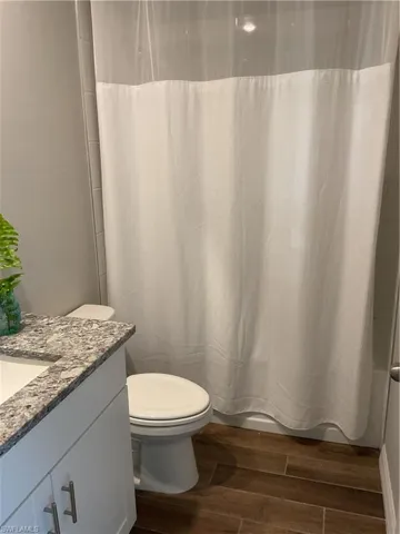 Full bath with shower / bath combination with curtain, toilet, vanity, and wood finish floors