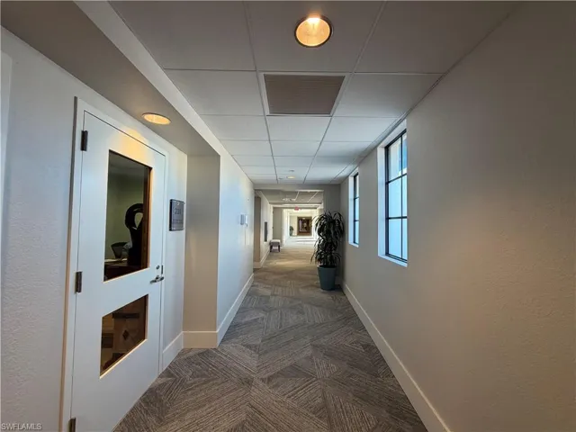 Corridor featuring textured walls, patterned carpet flooring, recessed lighting, and windows with dark trim