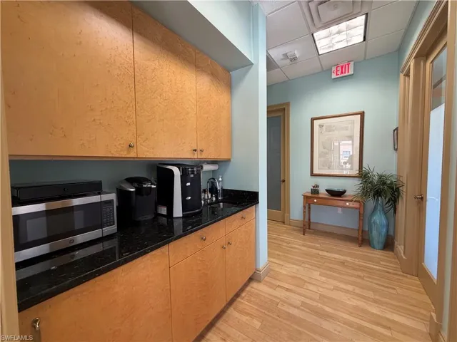 Compact kitchenette featuring wood-finish cabinetry, black granite-style countertops, and light wood-finish flooring