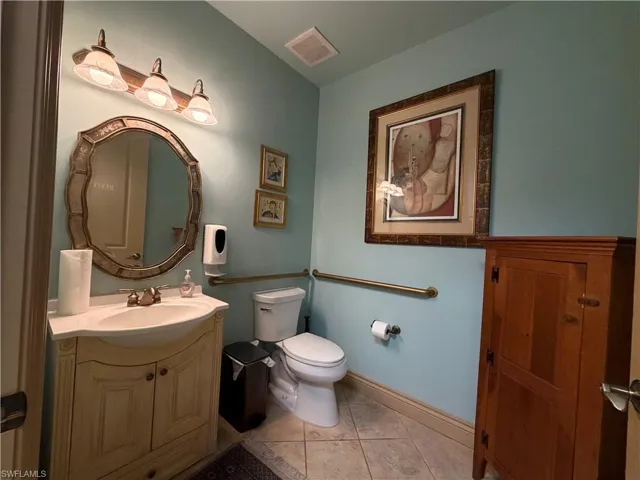 Powder room featuring a decorative vanity with an integrated sink, an ornate mirror, a three-light vanity fixture, and tiled flooring