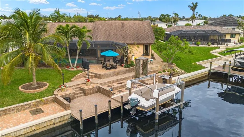 Dock area featuring glass enclosure, a lawn, a water view, and a patio