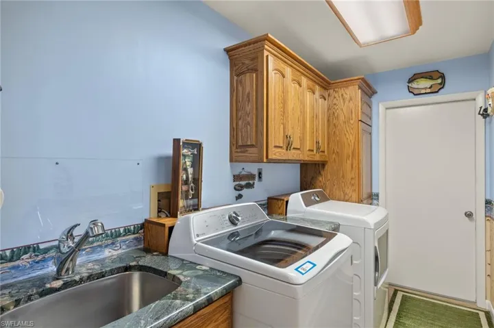 Clothes washing area with washer and clothes dryer, sink, and cabinets