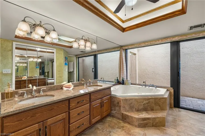 Bathroom with vanity, a tray ceiling, ornamental molding, and tiled tub
