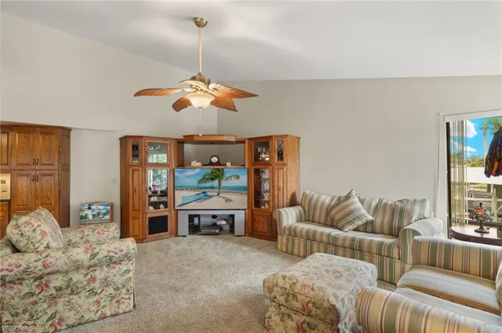Carpeted living room featuring ceiling fan and vaulted ceiling