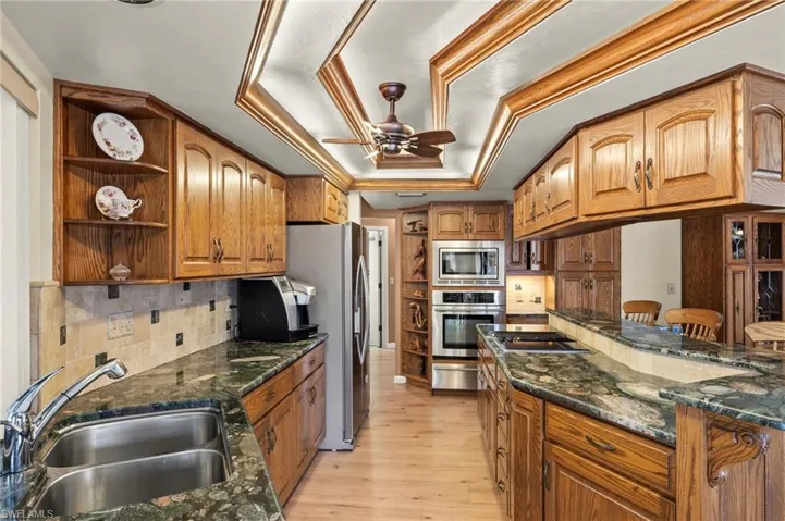 Kitchen featuring appliances with stainless steel finishes, sink, backsplash, a raised ceiling, and light wood-type flooring