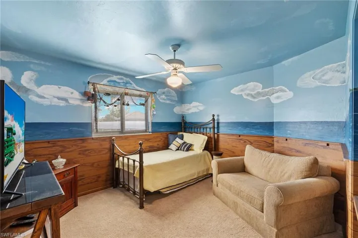 Carpeted bedroom featuring ceiling fan and wood walls