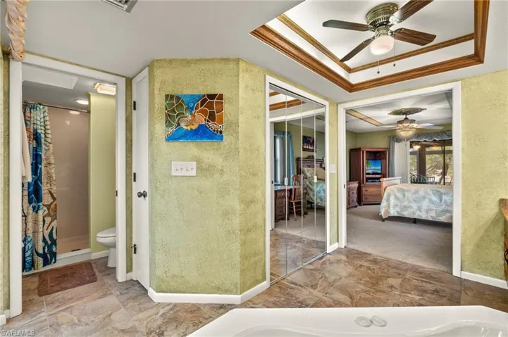 Bathroom featuring a shower with curtain, toilet, a raised ceiling, ceiling fan, and crown molding