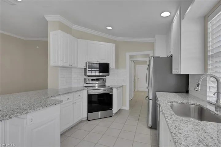 White cabinetry, stainless steel appliances, granite countertops, subway tile backsplash, and recessed lighting