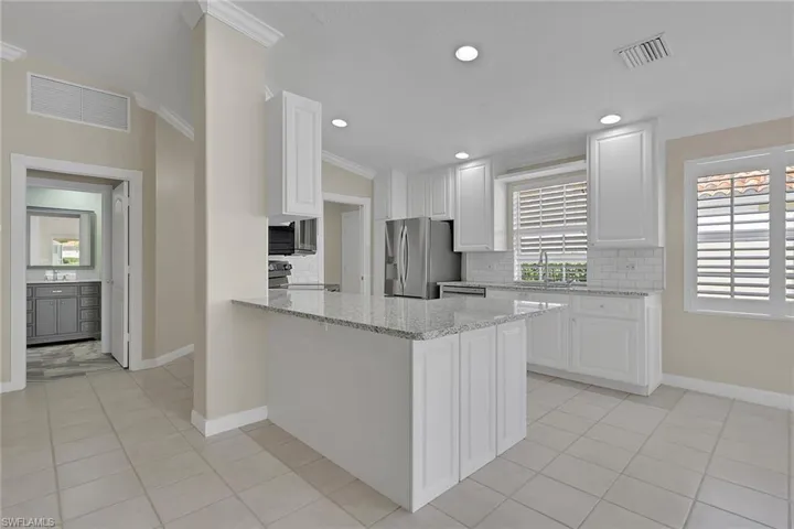 White shaker-style cabinetry, stainless steel appliances, granite countertops, tile flooring, and plantation shutters