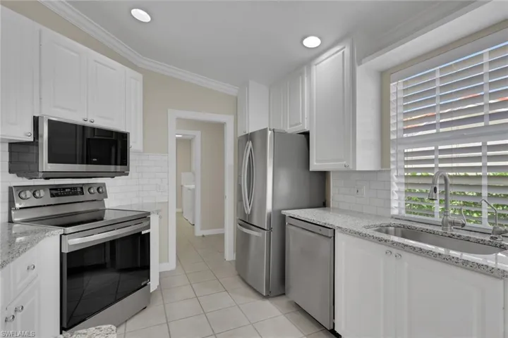 White shaker-style cabinetry, granite countertops, subway tile backsplash, stainless steel appliances, and tiled flooring
