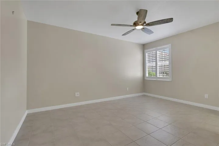 Neutral wall paint, ceiling fan with integrated lighting, window with white plantation shutters, and square tile flooring