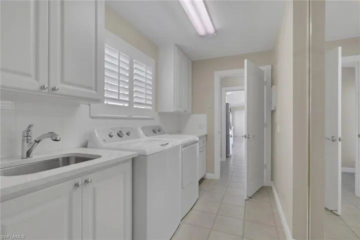 Laundry area featuring white cabinetry, a utility sink, white tile backsplash, and plantation shutters