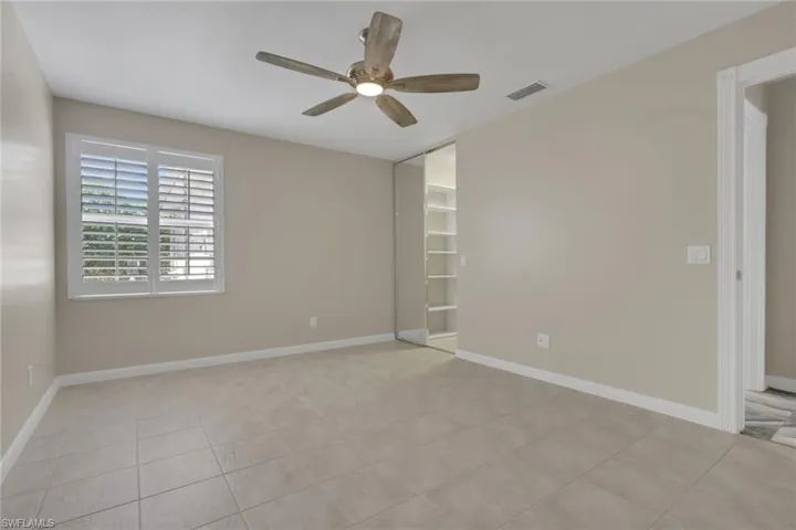 Light-toned tile flooring, white plantation shutters, and a wood-finish ceiling fan