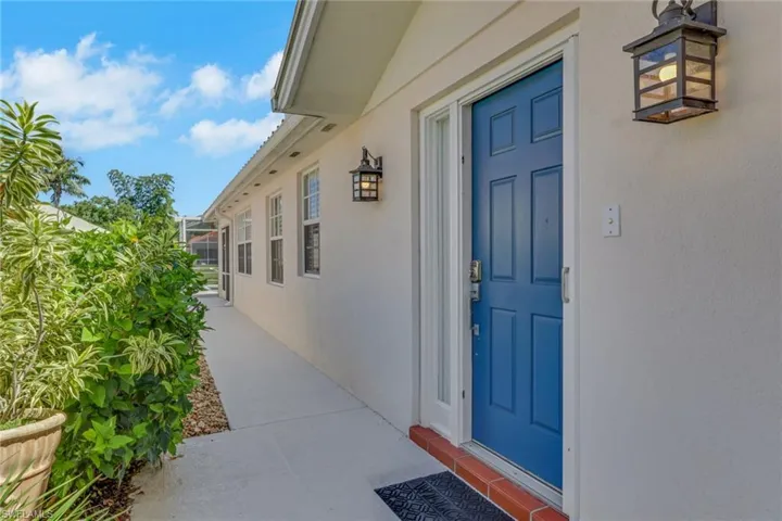 White exterior with a blue paneled entry door, flanked by a contemporary wall sconce and multiple windows