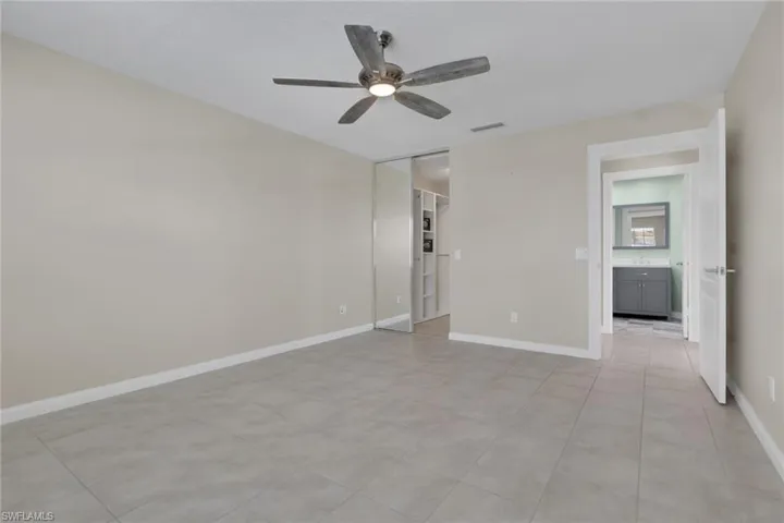 Light gray tile flooring with a neutral wall color, overhead ceiling fan, and built-in closet with mirrored sliding doors