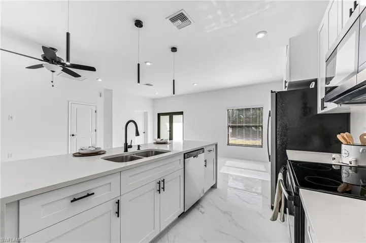 Kitchen featuring pendant lighting, white cabinets, sink, stainless steel dishwasher, and light stone counters