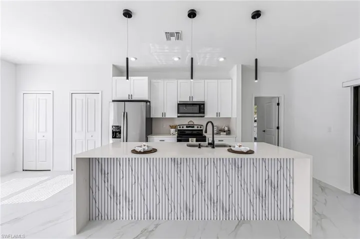 Kitchen with a center island with sink, white cabinets, decorative light fixtures, and appliances with stainless steel finishes