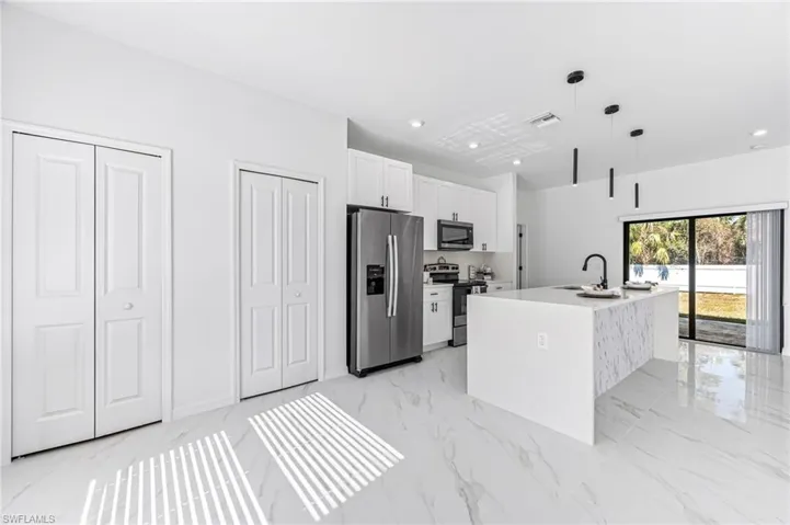 Kitchen featuring white cabinets, sink, an island with sink, appliances with stainless steel finishes, and decorative light fixtures