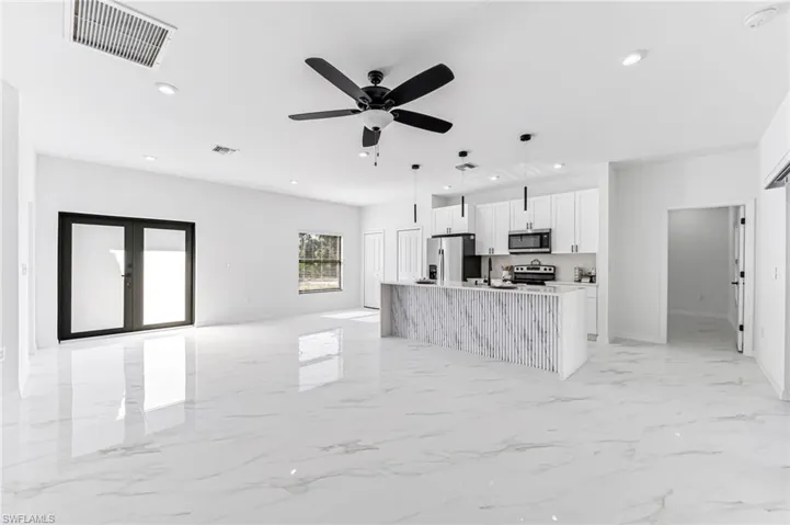 Kitchen featuring a kitchen island with sink, hanging light fixtures, ceiling fan, appliances with stainless steel finishes, and white cabinetry