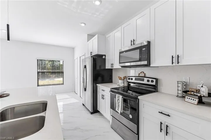 Kitchen with light stone counters, sink, white cabinetry, and stainless steel appliances