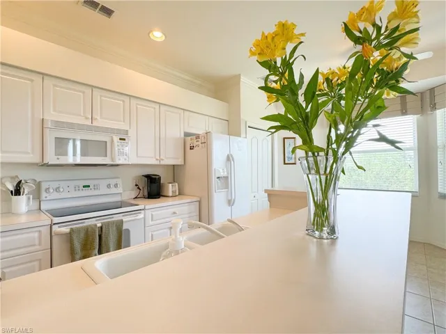 Kitchen with white appliances, light tile patterned floors, crown molding, sink, and white cabinets