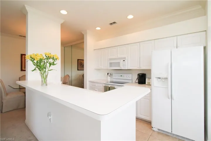 Kitchen featuring white appliances, light tile patterned floors, white cabinetry, and ornamental molding