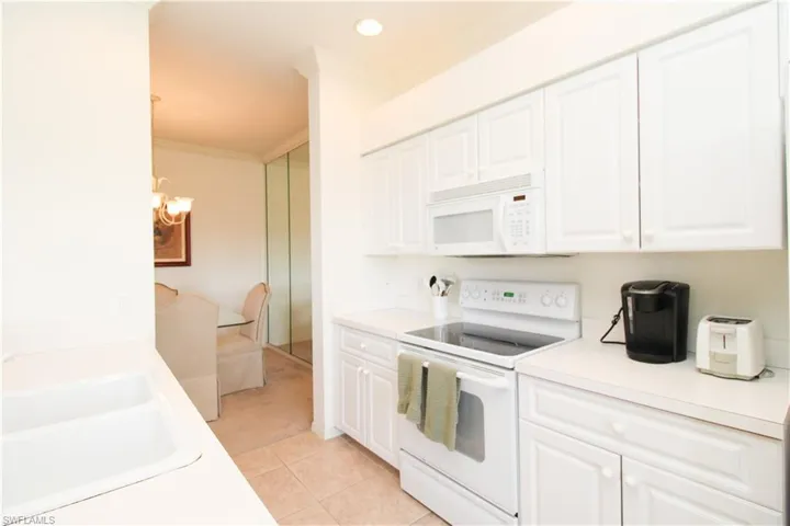 Kitchen featuring white cabinets, white appliances, light tile patterned floors, and ornamental molding