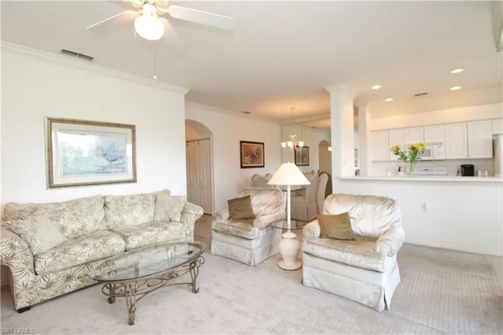 Carpeted living room with ornamental molding and ceiling fan with notable chandelier