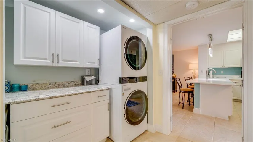 White shaker-style cabinetry with brushed nickel hardware, granite countertop, and stacked laundry appliances