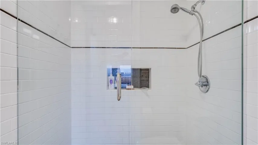 Glass-enclosed shower featuring white subway tile, a dark accent tile line, a recessed niche, and a chrome shower system