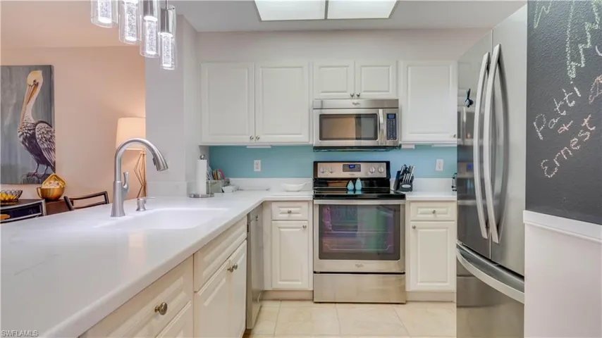 Kitchen featuring white cabinetry, light-toned countertops, stainless steel appliances, and a blue tile backsplash