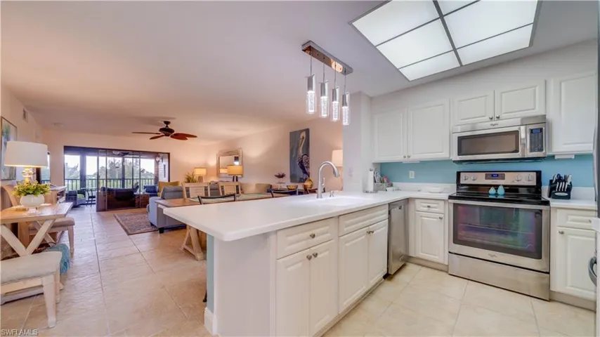 White cabinetry with stainless steel appliances, white countertops, modern pendant lighting, and tiled flooring