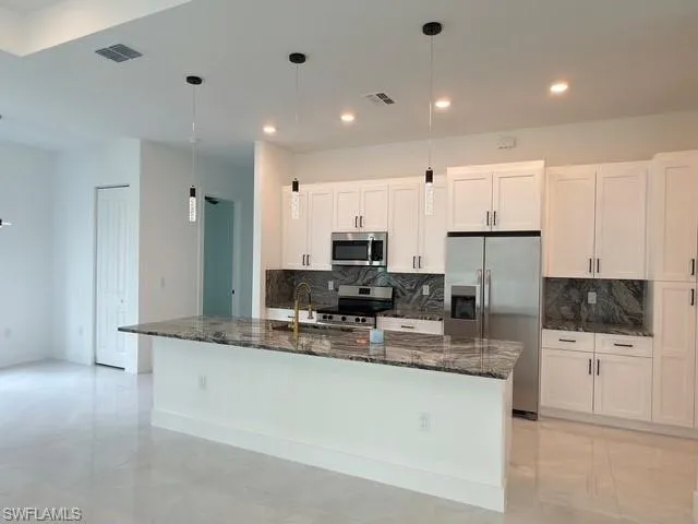 Kitchen featuring pendant lighting, white cabinetry, backsplash, and dark stone countertops