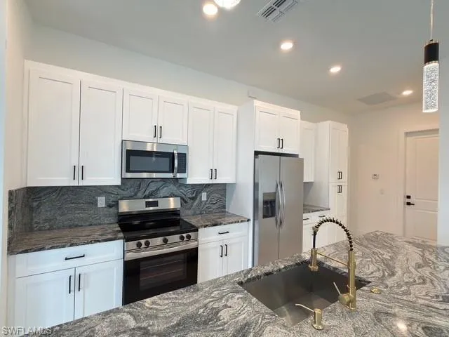 Kitchen featuring backsplash, dark stone counters, stainless steel appliances, white cabinetry, and decorative light fixtures