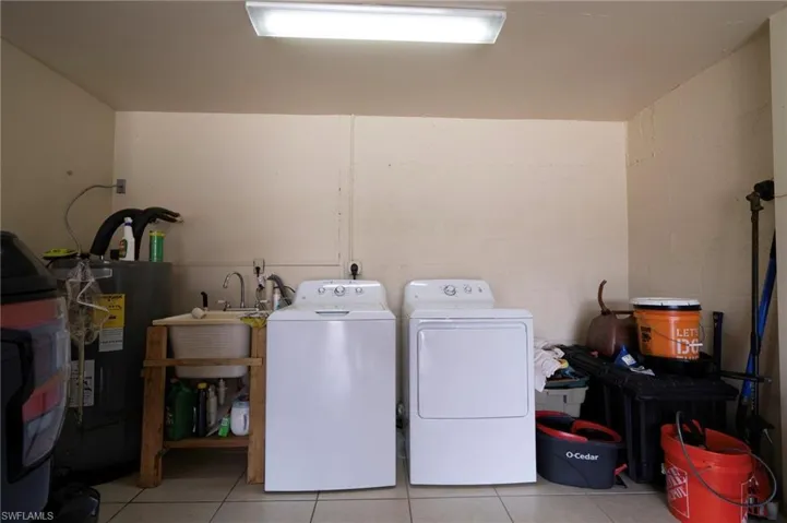 Laundry area featuring light tile patterned flooring, washing machine and dryer, and electric water heater