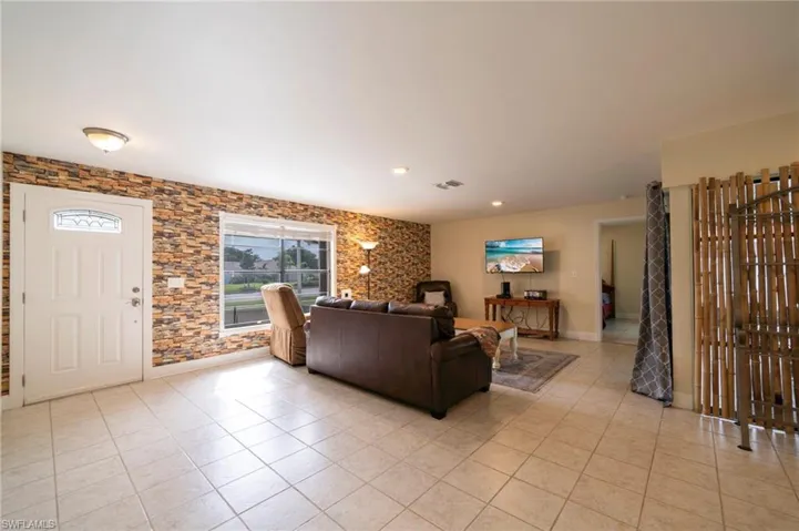 Living room featuring light tile patterned flooring, recessed lighting, and an accent wall