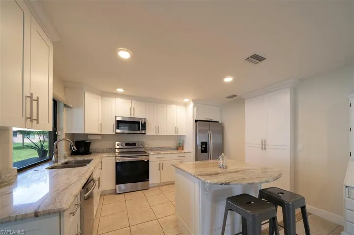 Kitchen featuring stainless steel appliances, light tile patterned floors, a breakfast bar area, white cabinets, and recessed lighting