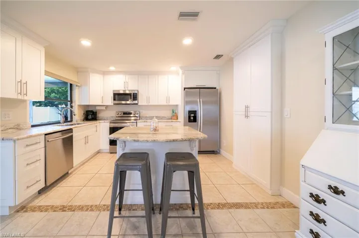 Kitchen featuring light tile patterned floors, white cabinets, appliances with stainless steel finishes, a kitchen breakfast bar, and recessed lighting