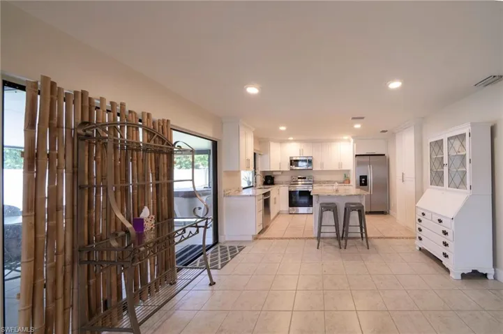 Kitchen featuring a kitchen bar, appliances with stainless steel finishes, white cabinetry, light tile patterned flooring, and recessed lighting