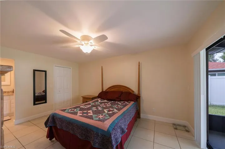 Bedroom featuring access to exterior, light tile patterned flooring, a ceiling fan, and ensuite bath