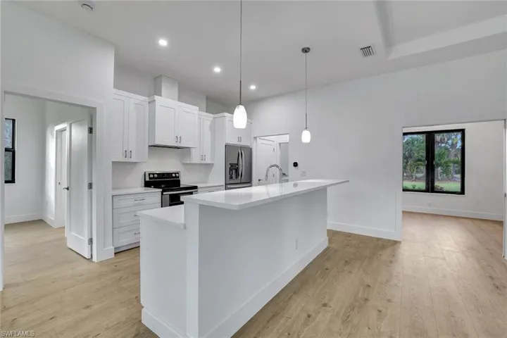 Kitchen featuring a kitchen island with sink, hanging light fixtures, appliances with stainless steel finishes, light hardwood / wood-style floors, and white cabinetry