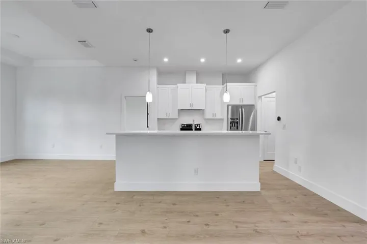 Kitchen with white cabinets, an island with sink, pendant lighting, and appliances with stainless steel finishes